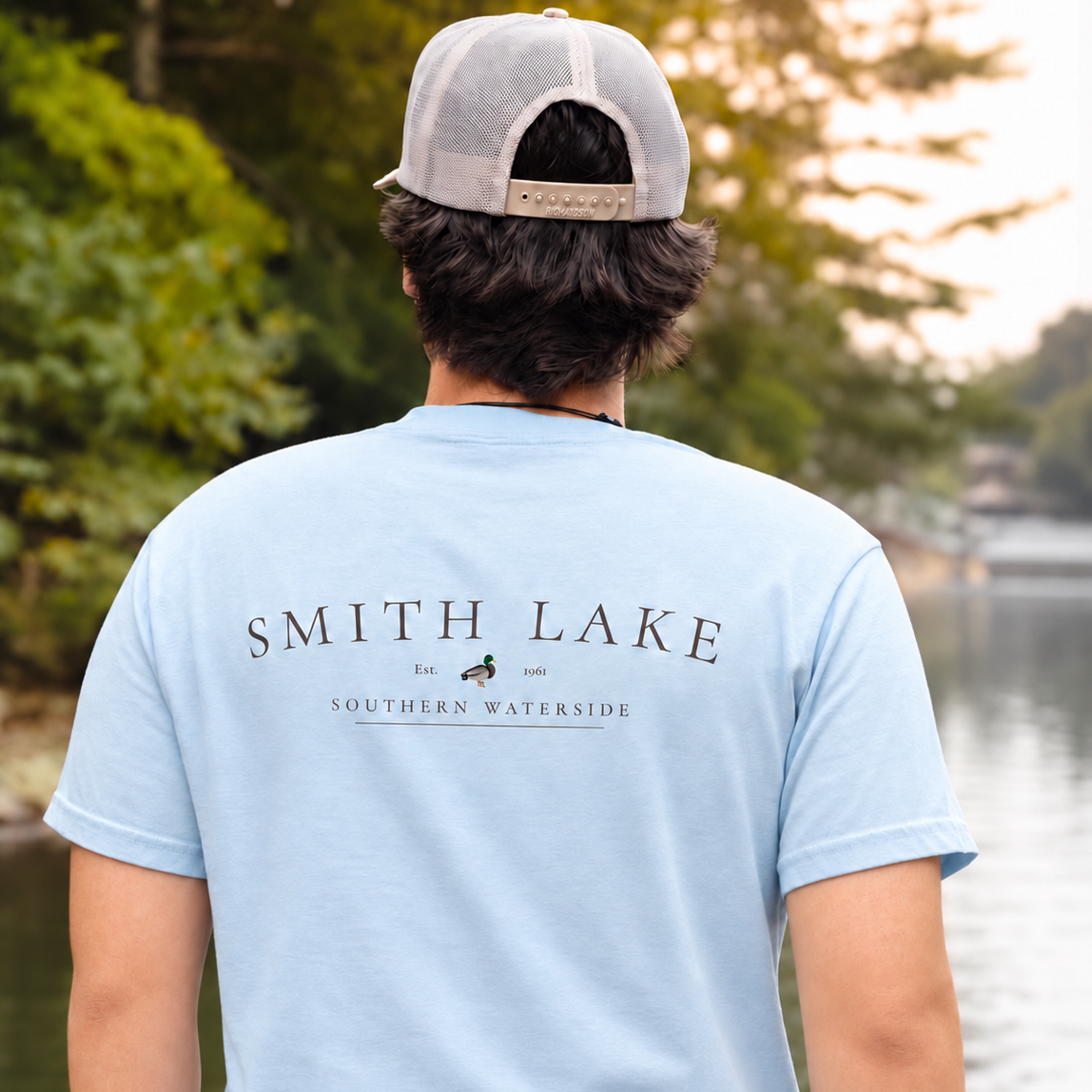 Man wearing a baby blue Smith Lake graphic T-shirt outdoors by the lake.